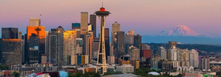 Seattle skyline at twilight featuring the iconic Space Needle and Mount Rainier in the background, showcasing a vibrant mix of modern skyscrapers reflecting warm sunset hues.
