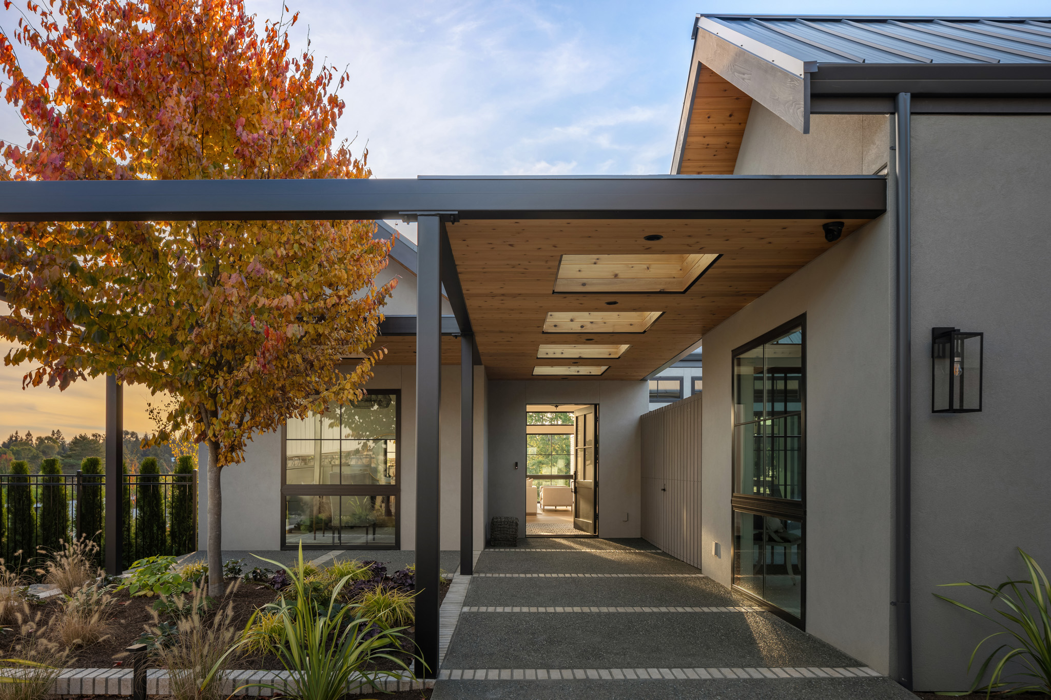 Modern exterior entrance of a contemporary home in the Pacific Northwest, featuring a stylish covered walkway, autumn foliage, and sleek landscaping elements.