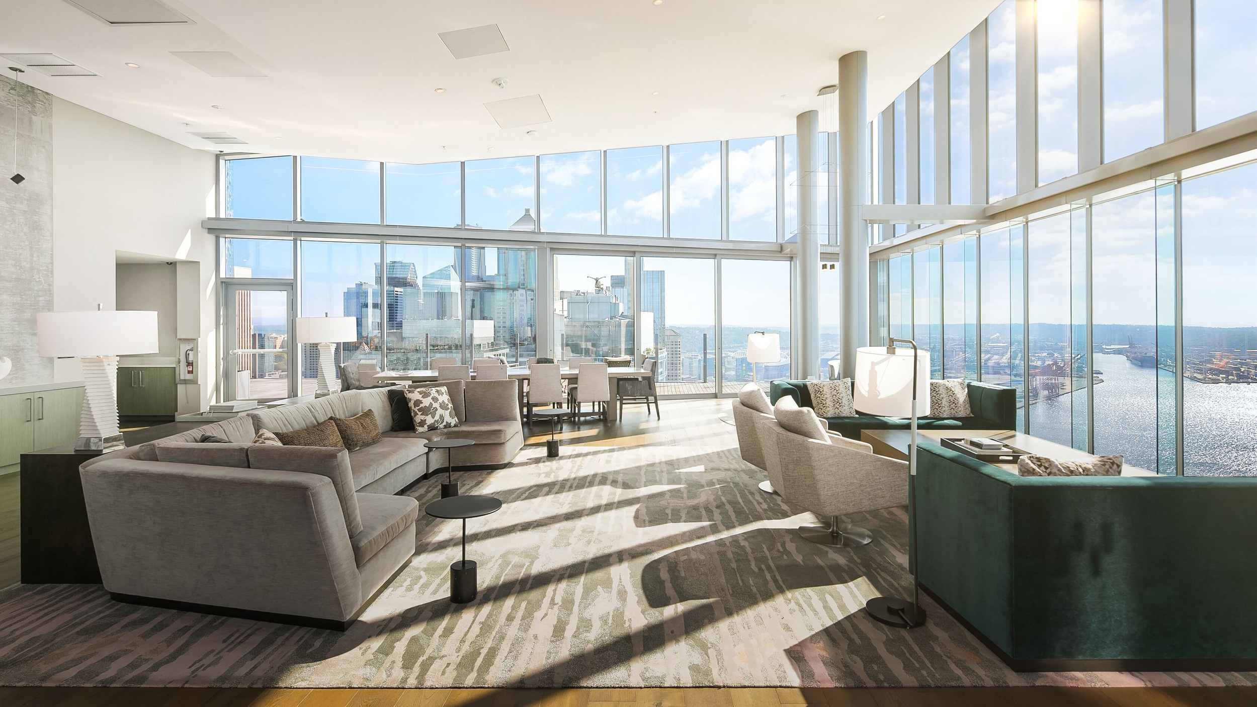 Modern living room with expansive windows offering stunning views of Seattle's skyline and waterfront, featuring elegant furnishings and a bright, airy atmosphere.