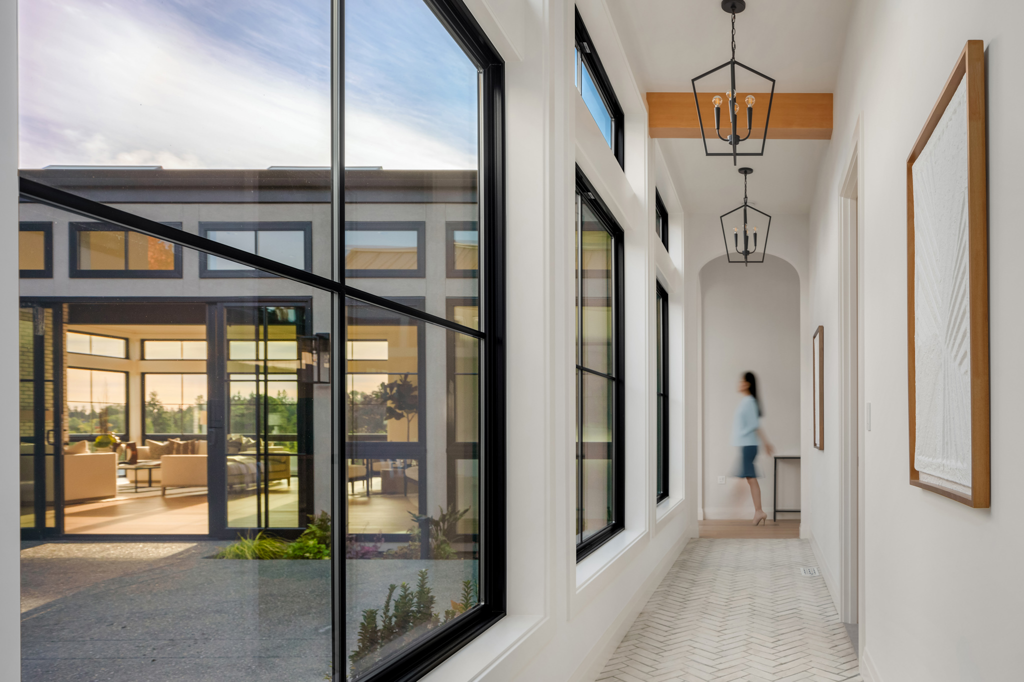 Bright and modern hallway featuring large black-framed windows, elegant light fixtures, and herringbone flooring, showcasing a view of a stylish living area in the Pacific Northwest.