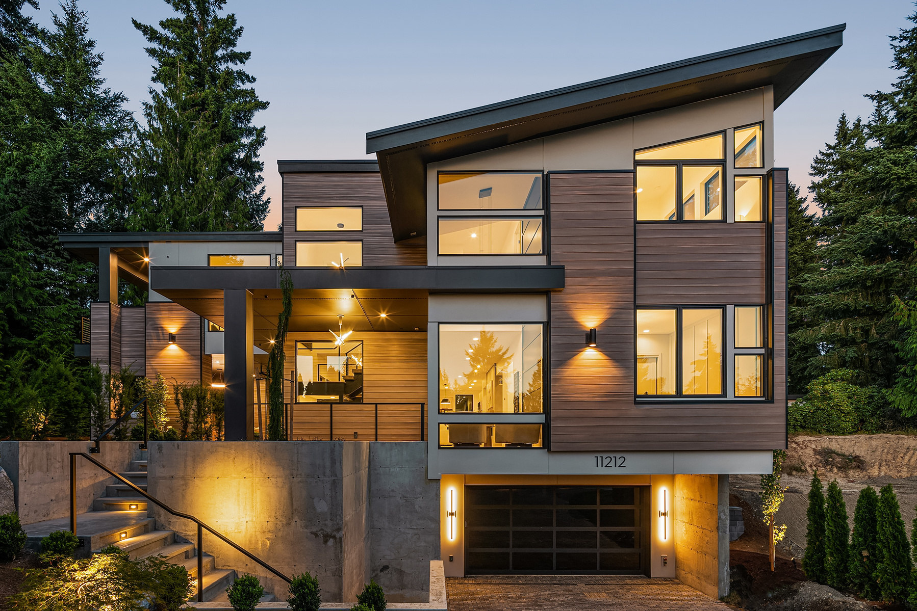 Modern exterior of a luxury home featuring large windows and contemporary design elements, surrounded by lush greenery in the Pacific Northwest.