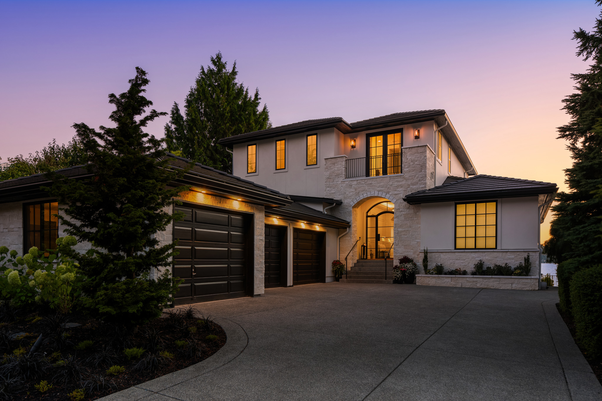 Modern exterior of a luxury home at twilight in the Pacific Northwest, featuring elegant architectural details, warm lighting, and a landscaped driveway.