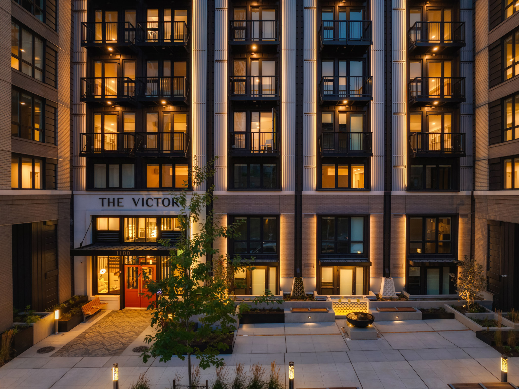 Modern exterior view of The Victor apartment building in Seattle, featuring stylish balconies and warm ambient lighting, creating an inviting atmosphere in the evening.