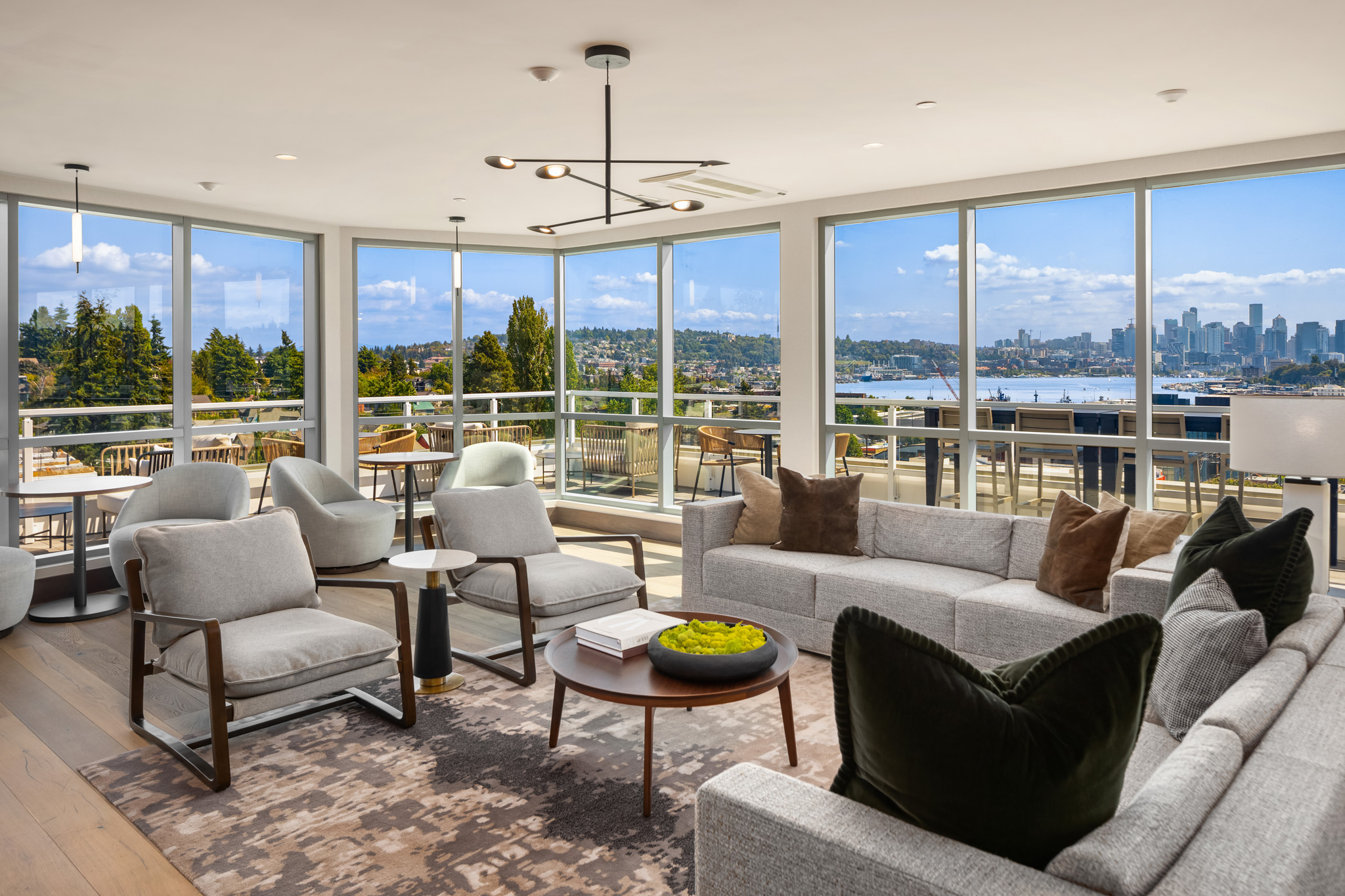 Modern living room with panoramic views of Seattle, featuring a stylish sectional sofa, elegant accent chairs, and a round coffee table, creating a bright and inviting atmosphere.