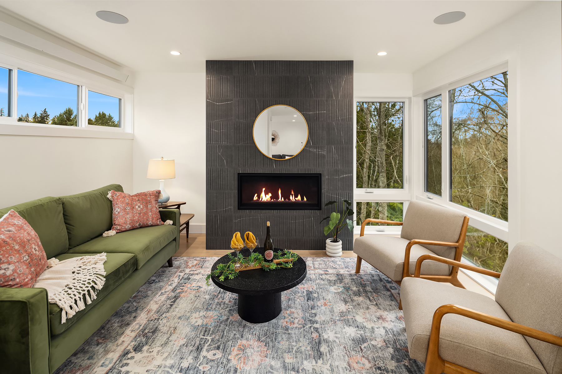 Modern living room with a sleek fireplace and large windows, featuring a green sofa with floral accents and minimalist decor, located in the Pacific Northwest.