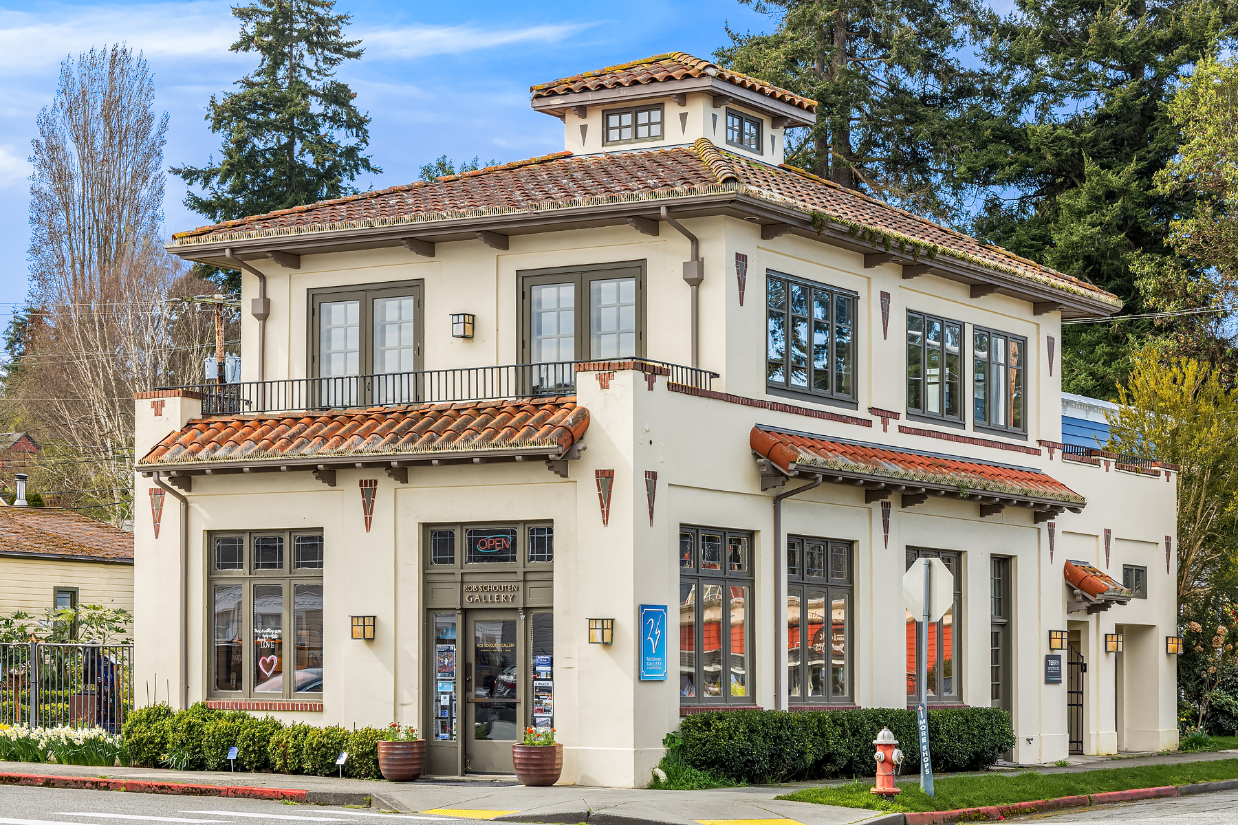 Charming exterior of a Mediterranean-style gallery building in the Pacific Northwest, featuring terracotta roof tiles, large windows, and elegant architectural details amidst lush greenery.