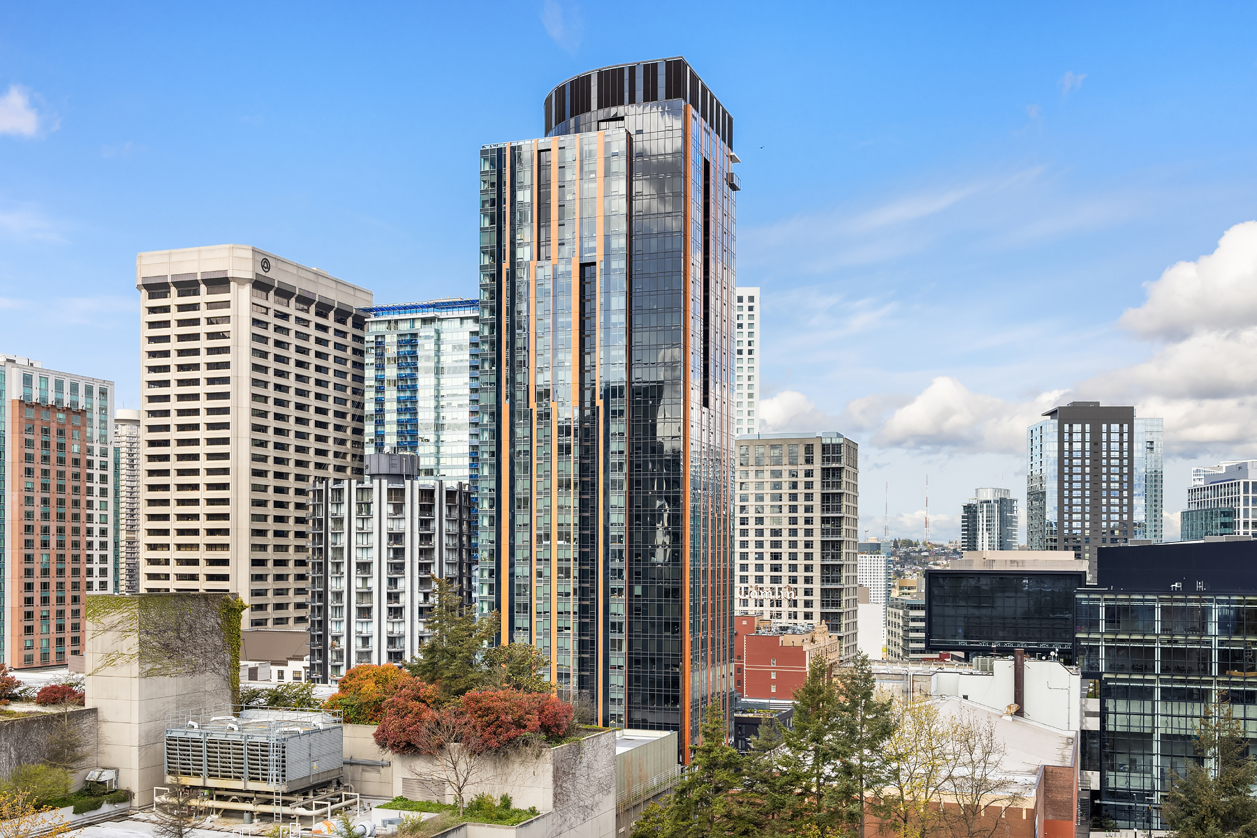 Modern high-rise building in Seattle's skyline featuring sleek glass and wood accents against a clear blue sky, showcasing urban living at its finest.