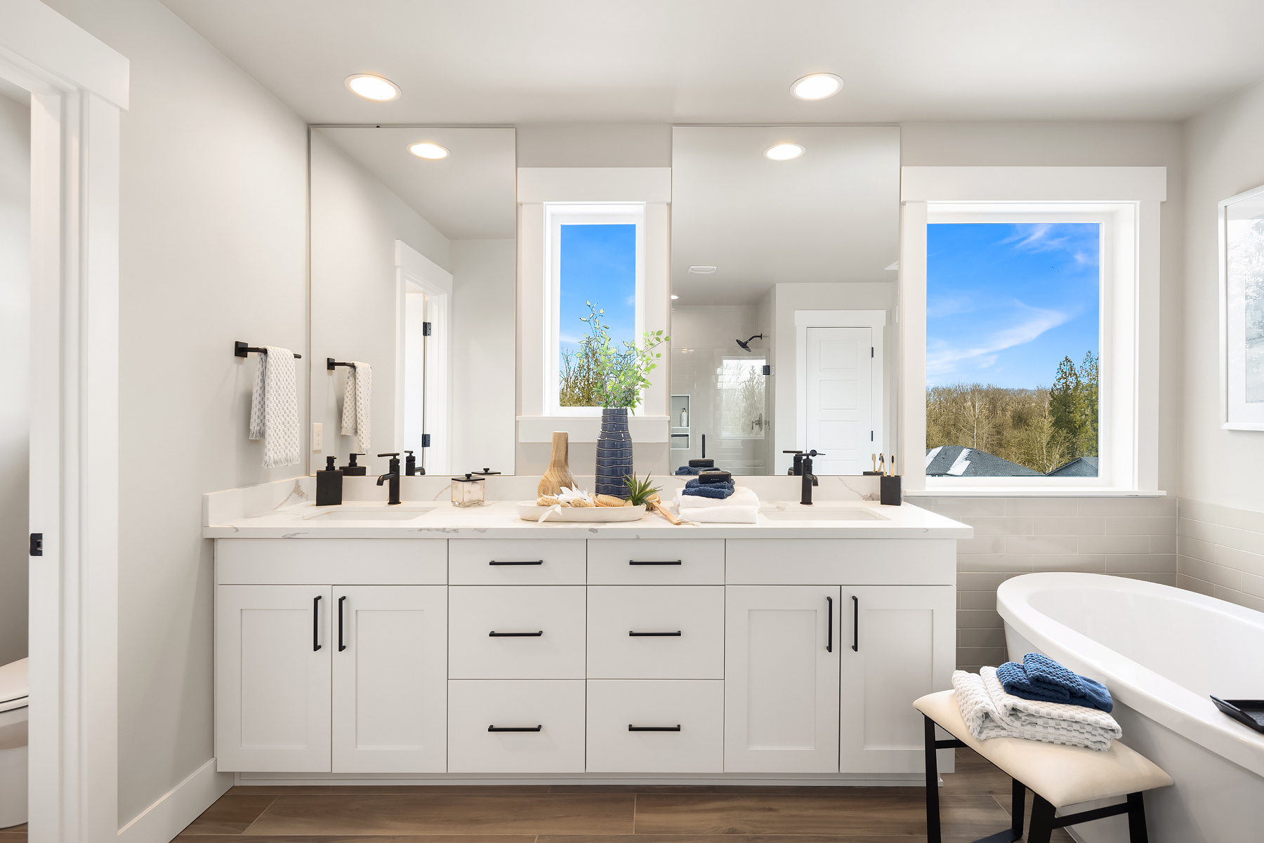 Modern bathroom featuring sleek white cabinetry, black fixtures, and large mirrors, complemented by natural light from windows overlooking a serene landscape, located in the Pacific Northwest.