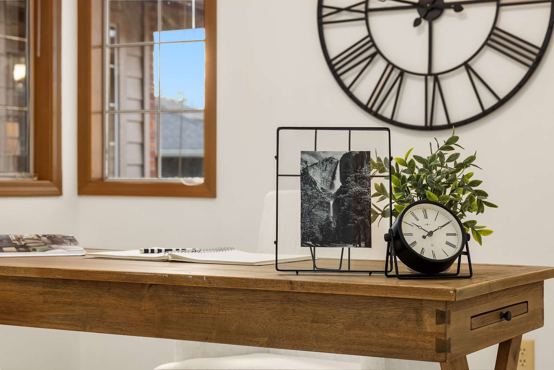 Modern home office space featuring a wooden desk adorned with decorative elements, including a clock and a framed photograph, set against bright windows in a Pacific Northwest residence.