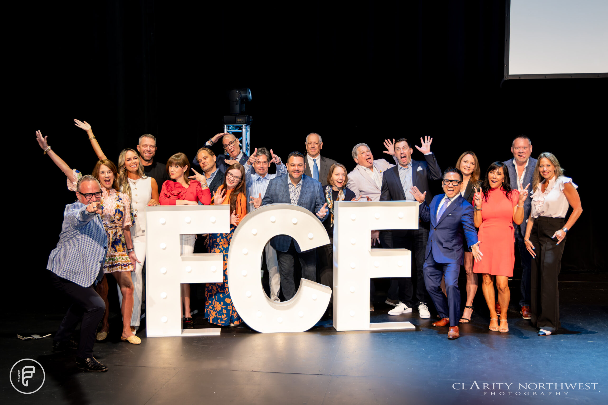 Group of real estate professionals posing playfully on stage with large illuminated letters spelling "ECE," captured in a lively atmosphere during an event with clarity's professional event photography in seattle