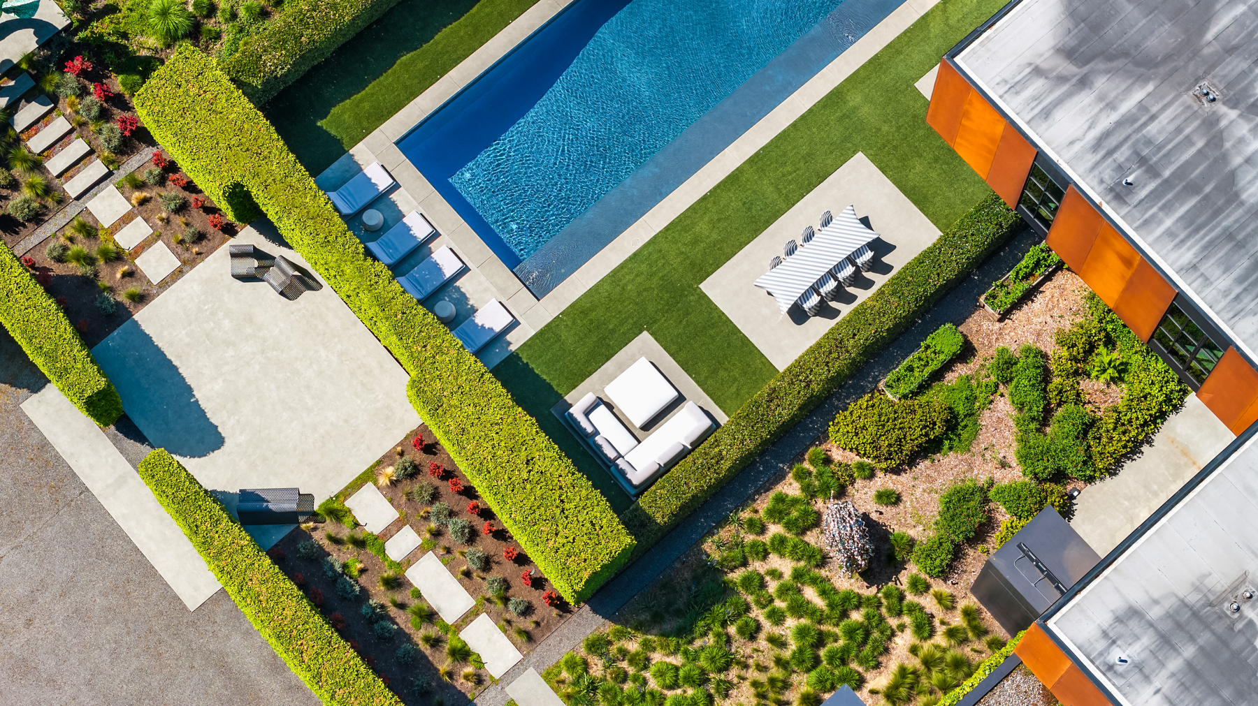 Triptych Bellevue $79M. Aerial view of a modern outdoor living space featuring a sleek swimming pool, manicured landscaping, and stylish seating areas in a vibrant, sunny setting in the Pacific Northwest.