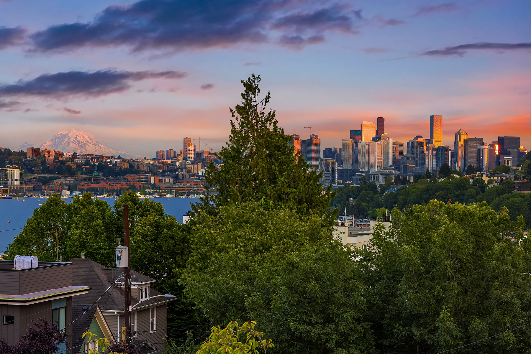 Stunning view of Seattle's skyline at twilight, featuring Mount Rainier in the background and lush greenery in the foreground, showcasing a vibrant blend of urban and natural beauty.
